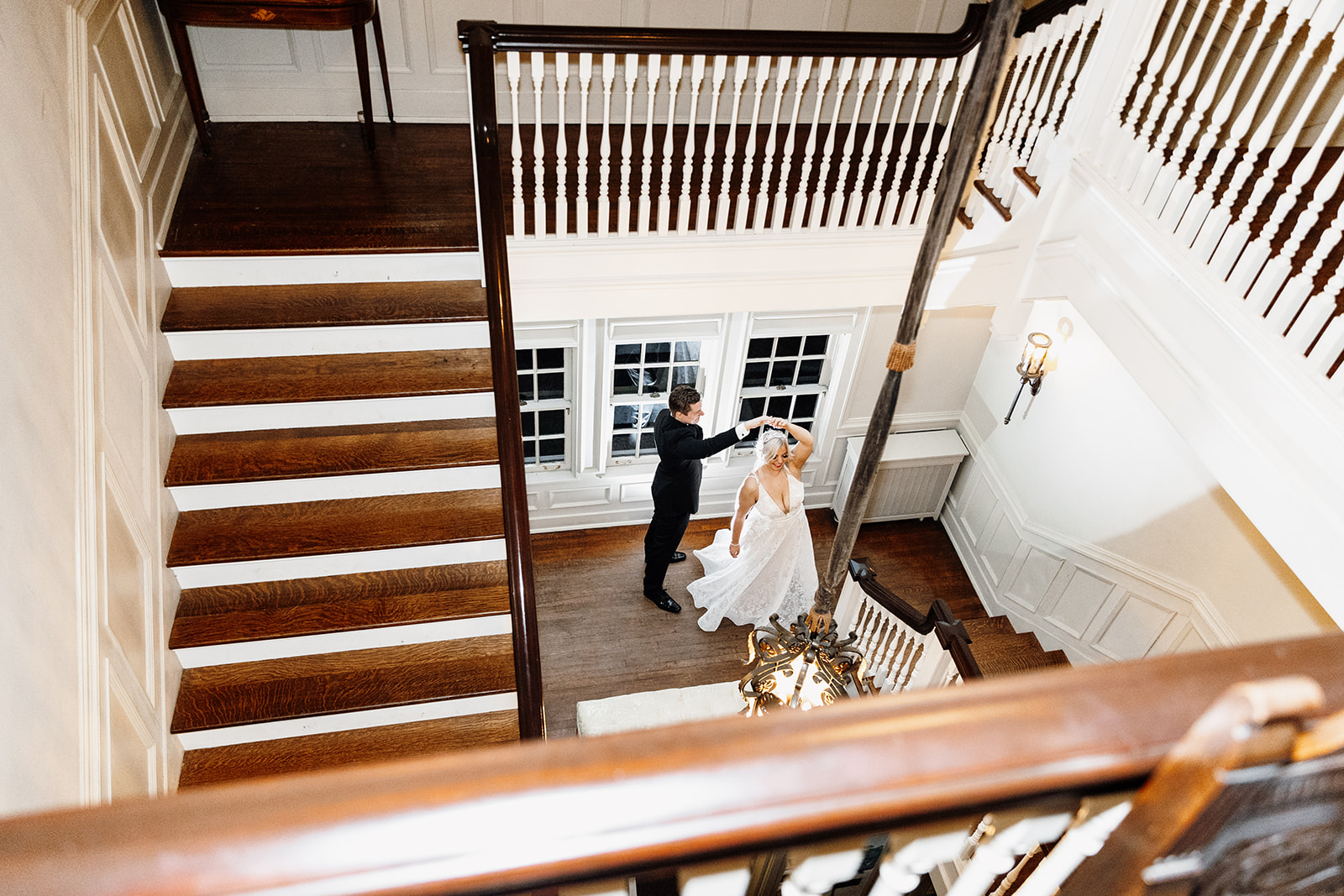 A bride and groom dance together at the bottom of a wooden staircase in a bright, elegant interior—one of the stunning scenes you’ll find at top Chicago wedding venues, viewed from above.