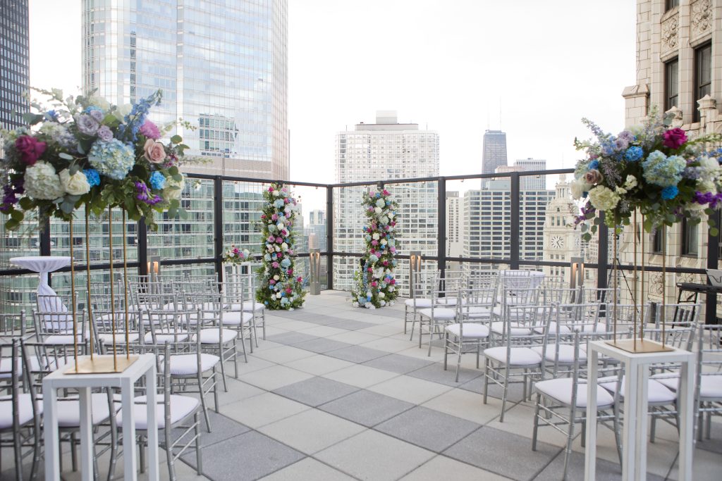 Outdoor rooftop wedding setup with rows of silver chairs, elegant floral arrangements, and city skyscrapers in the background—perfect for couples seeking the best Chicago wedding venues.