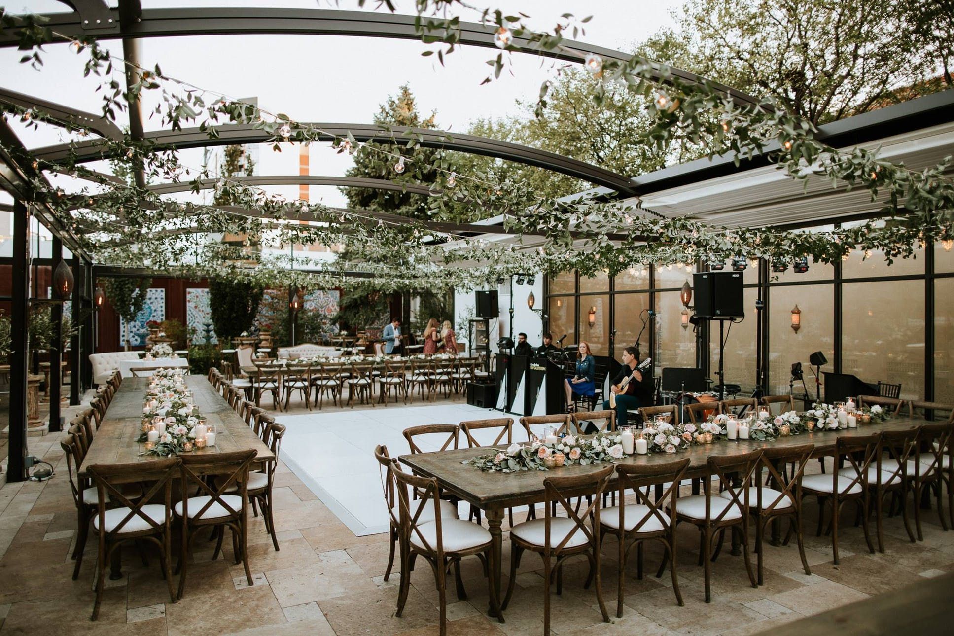 An outdoor event space among top Chicago wedding venues, featuring long wooden tables with floral arrangements, a white dance floor, overhead greenery, and a live band setting up in the background.