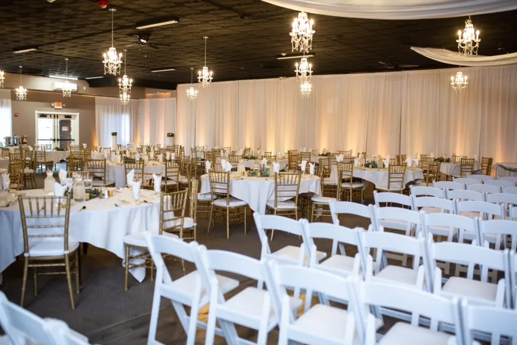 A banquet hall set up for an event with round tables covered in white cloths, gold chairs, rows of white chairs, chandeliers, and draped white fabric on the ceiling—perfect inspiration for elegant Chicago wedding venues.