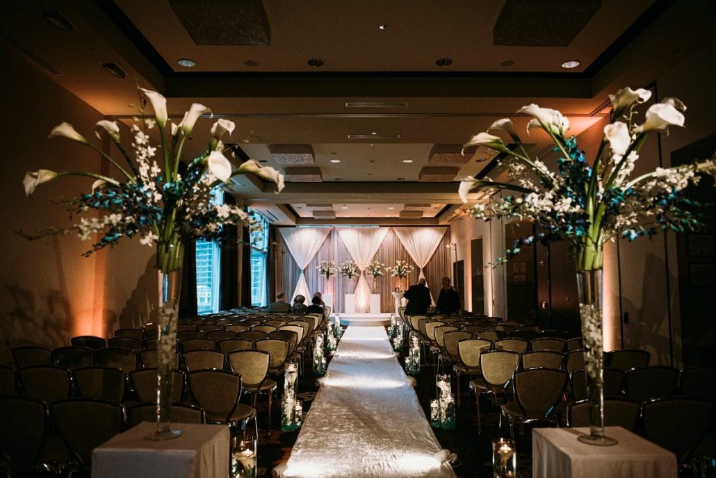 In dimly lit Chicago wedding venues, rows of chairs face a beautifully decorated altar. Tall floral arrangements and a pristine white aisle runner guide guests to the enchanting ceremony at the front.